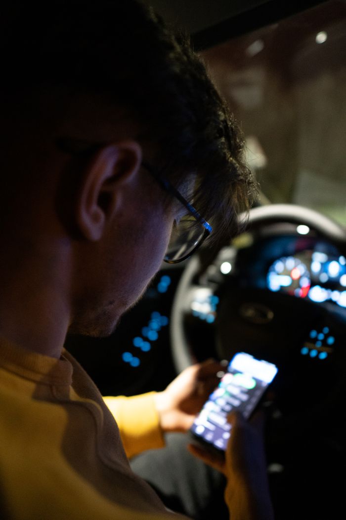 Services Person using a smartphone inside a car at night, focusing on technology and safety.