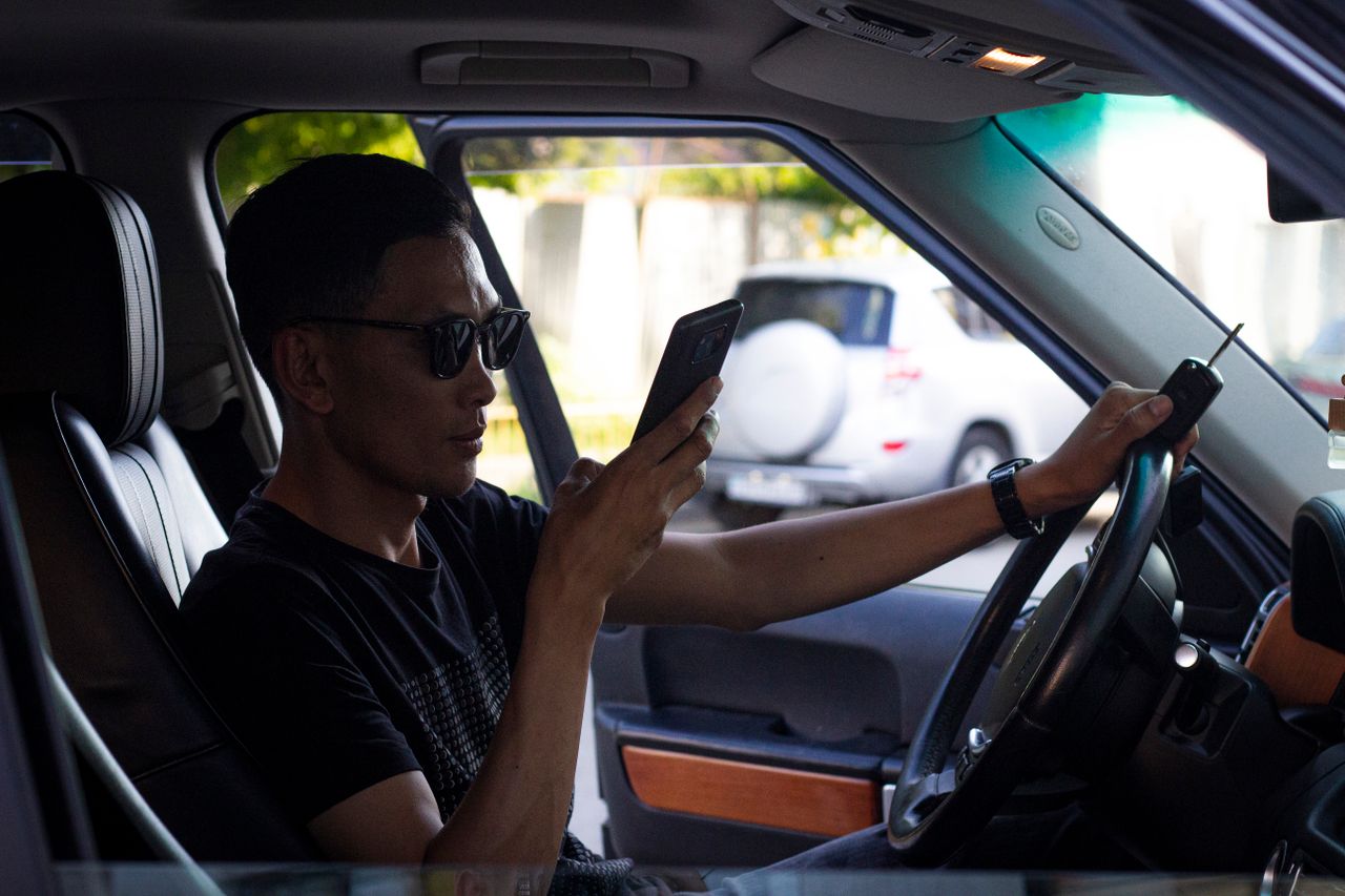 A propos Man wearing sunglasses using a smartphone while sitting in a car. Modern car interior and technology use.