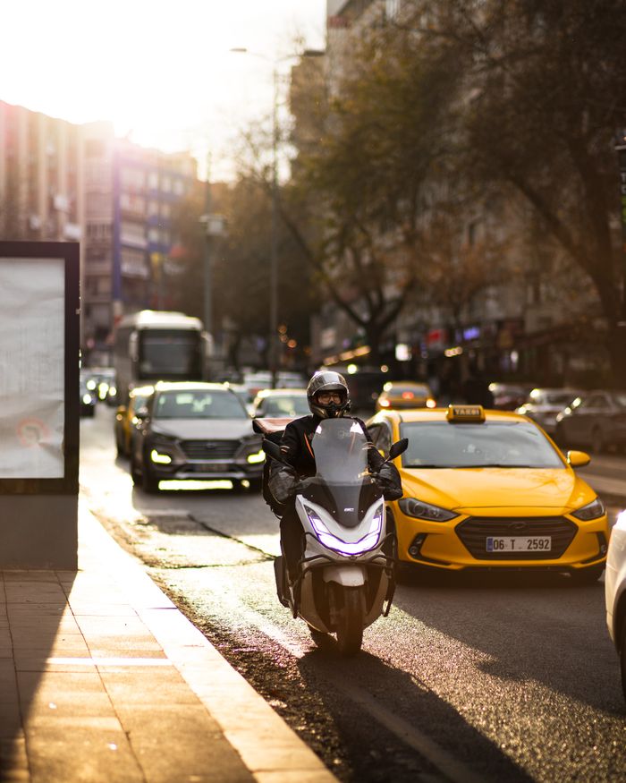 Motorcycle and taxi in bustling city street during sunset, capturing urban life.