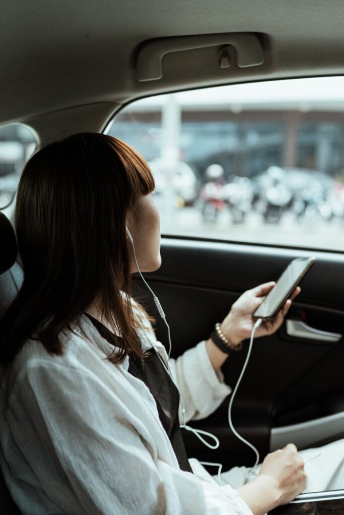 pexels photo 4429515 Side view unrecognizable female in casual outfit sitting in car passenger seat with cellphone and listening to favorite music in earphones against urban environment and looking out window